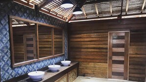 Un baño con tocador de madera, tres lavamanos blancos, un espejo grande y una puerta de madera.