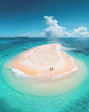 Eine Vogelperspektive einer kleinen, kreisförmigen Insel mit einem Sandstrand und klarem, türkisfarbenem Wasser.