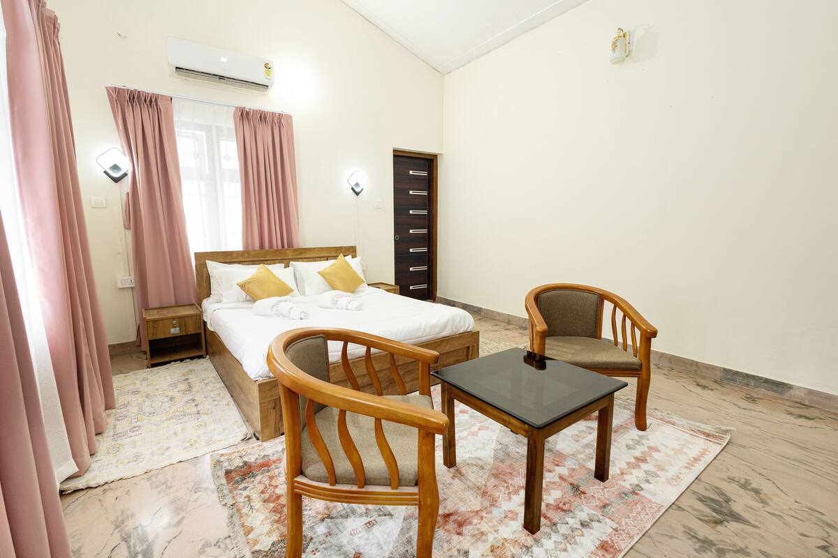 A bedroom with a bed, two wooden chairs, a small table, a nightstand, and a wardrobe.