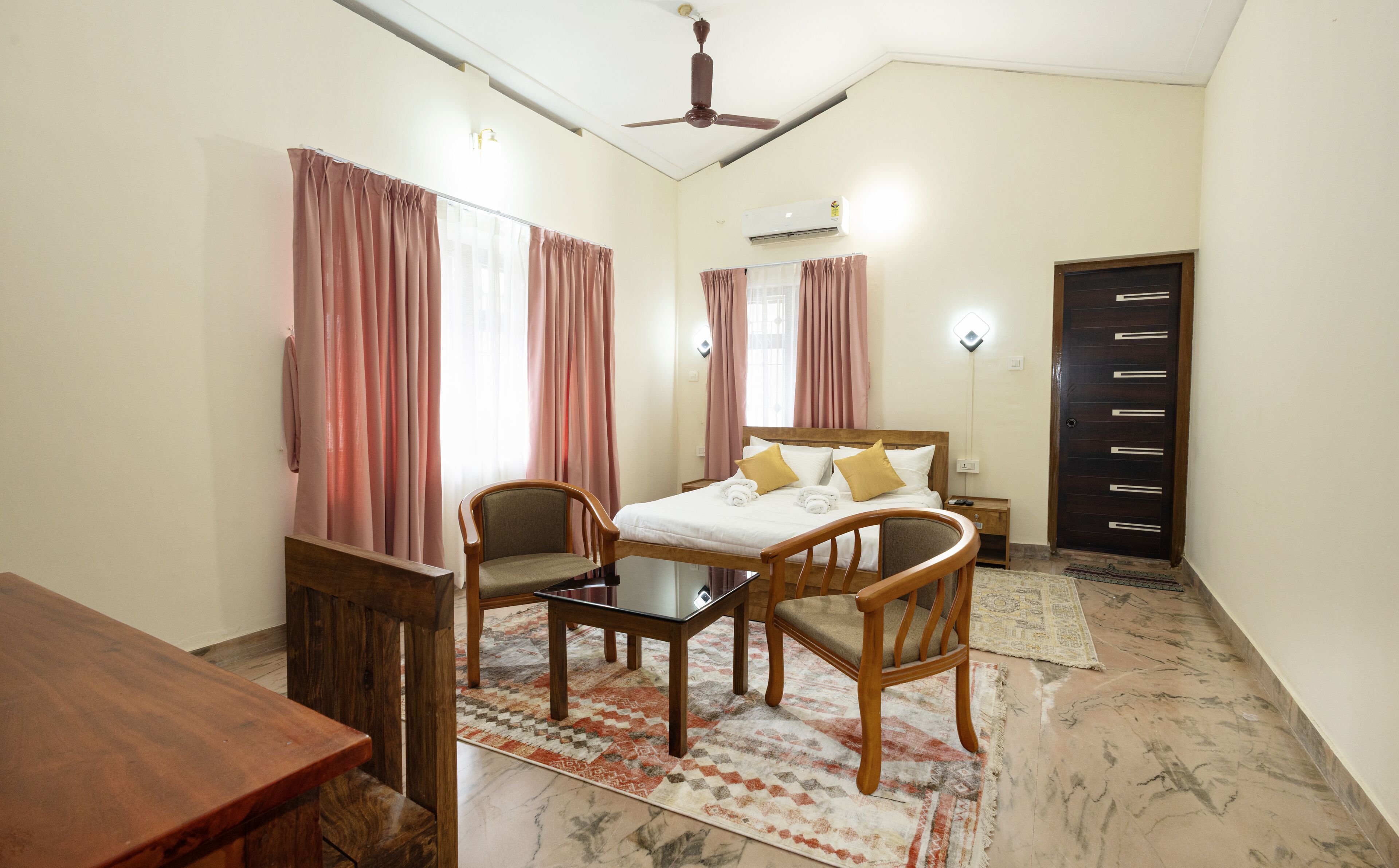 Une chambre d’hôtel avec un lit, deux chaises, une table, un climatiseur et une porte.