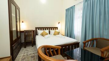 A hotel room with a bed, two chairs, a table, a wardrobe, and a window with curtains.