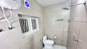 A small, modern bathroom with a toilet, a window with bars, a towel rack, and a shower area. - Bloom Fort Villa  (Kannur)