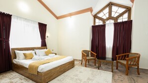 A bedroom with a wooden bed, two chairs, a small table, and a large window with curtains. - Bloom Fort Villa  (Kannur)