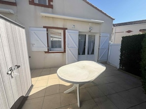 Ein Haus mit einer Terrasse, einem weißen Tisch und einer weißen Tür mit Fensterläden.