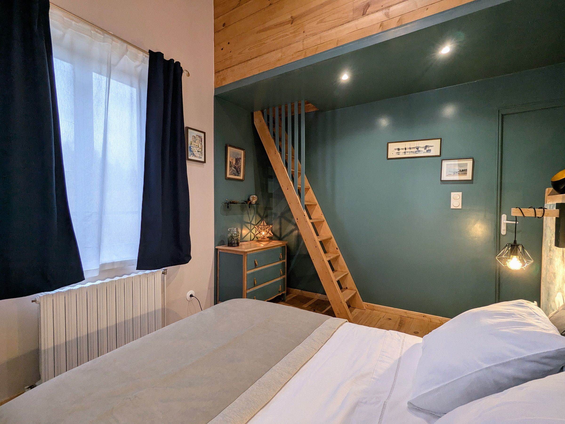 Une chambre à coucher avec un lit, une échelle en bois, une commode et un mur orné de tableaux.