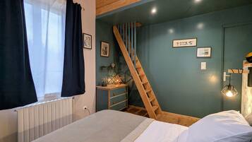 Une chambre à coucher avec un lit, une échelle en bois, une commode et un mur orné de tableaux.