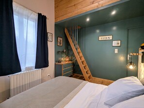 Une chambre à coucher avec un lit, une échelle en bois, une commode et un mur orné de tableaux.