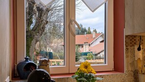 Una cocina con ventana, cafetera, planta en maceta y mantel estampado.