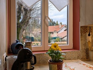 Une cuisine avec une fenêtre, une machine à café, une plante en pot et une nappe à motifs.