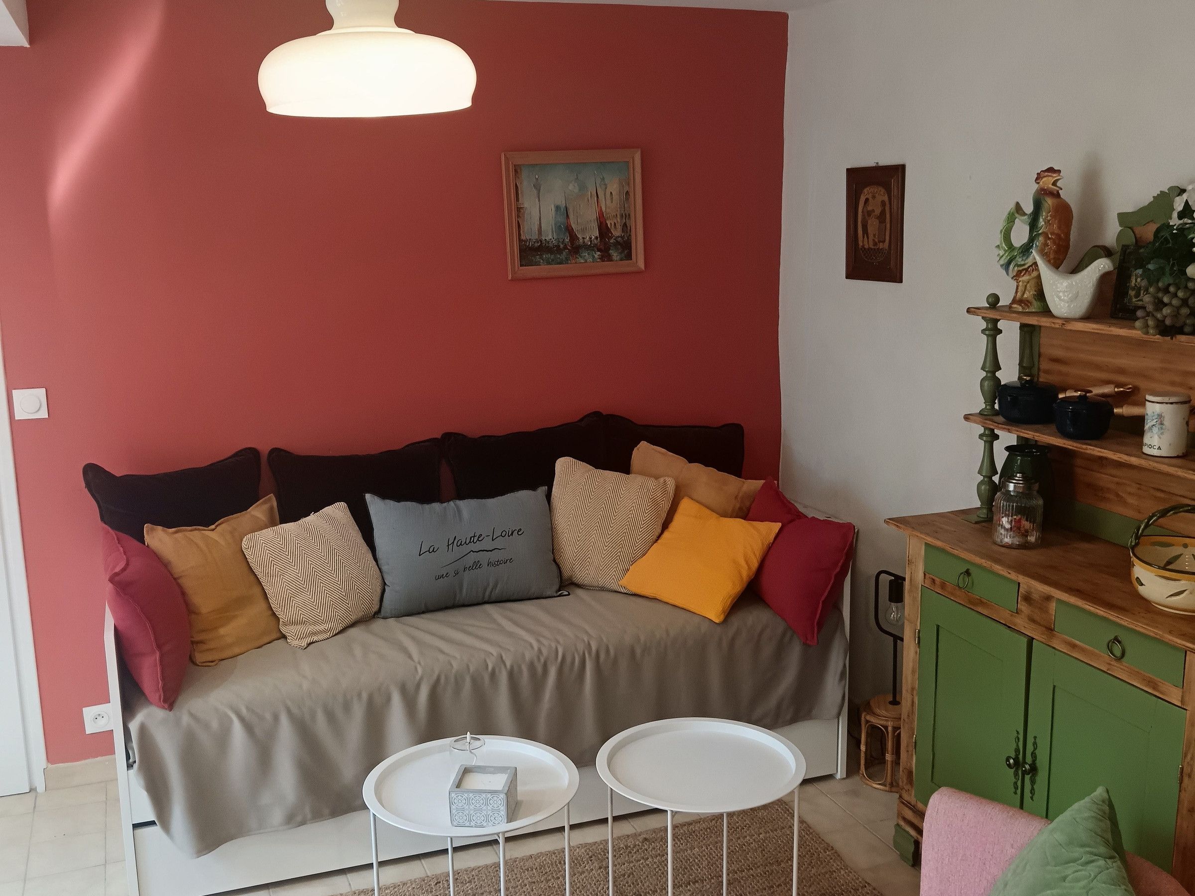 Un salon chaleureux avec un canapé, deux tables d’appoint, une suspension et une étagère murale agrémentée d’objets décoratifs.