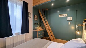 Un dormitorio con cama, una escalera de madera, un aparador y una pared con cuadros.