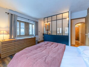 Ein Schlafzimmer mit einem Bett, einem Schminktisch, einem Fenster mit Vorhängen und einem Spiegel.