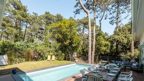 Area piscina con tavolo e sedie, circondata da un solarium in legno e una piscina.