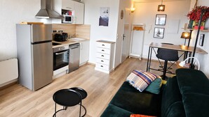 Eine moderne Küche mit integriertem Backofen, Mikrowelle und einem Edelstahlkühlschrank. Es gibt einen Essbereich mit Tisch und Stühlen sowie ein Wohnzimmer mit einem grünen Sofa und einem kleinen runden Tisch.
