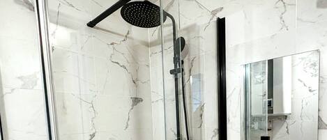 A modern bathroom with a glass-enclosed shower, a white sink, and a large mirror.