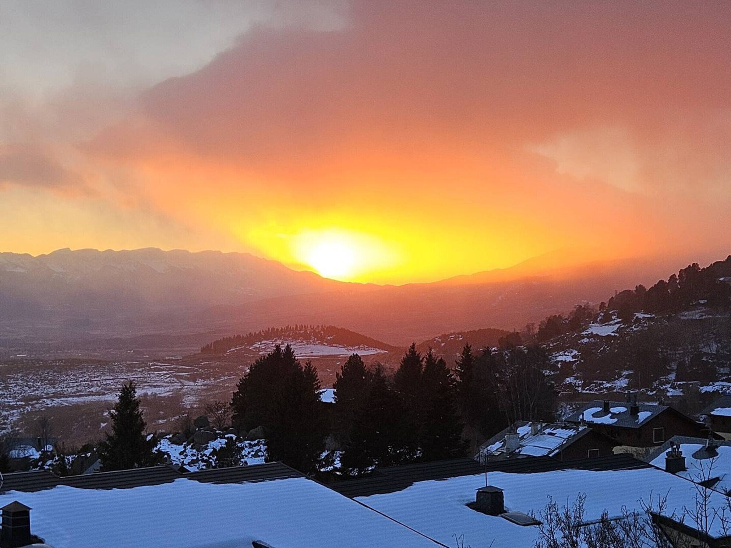 A mountainous landscape with a sunset, snow-covered houses, and a clear sky.