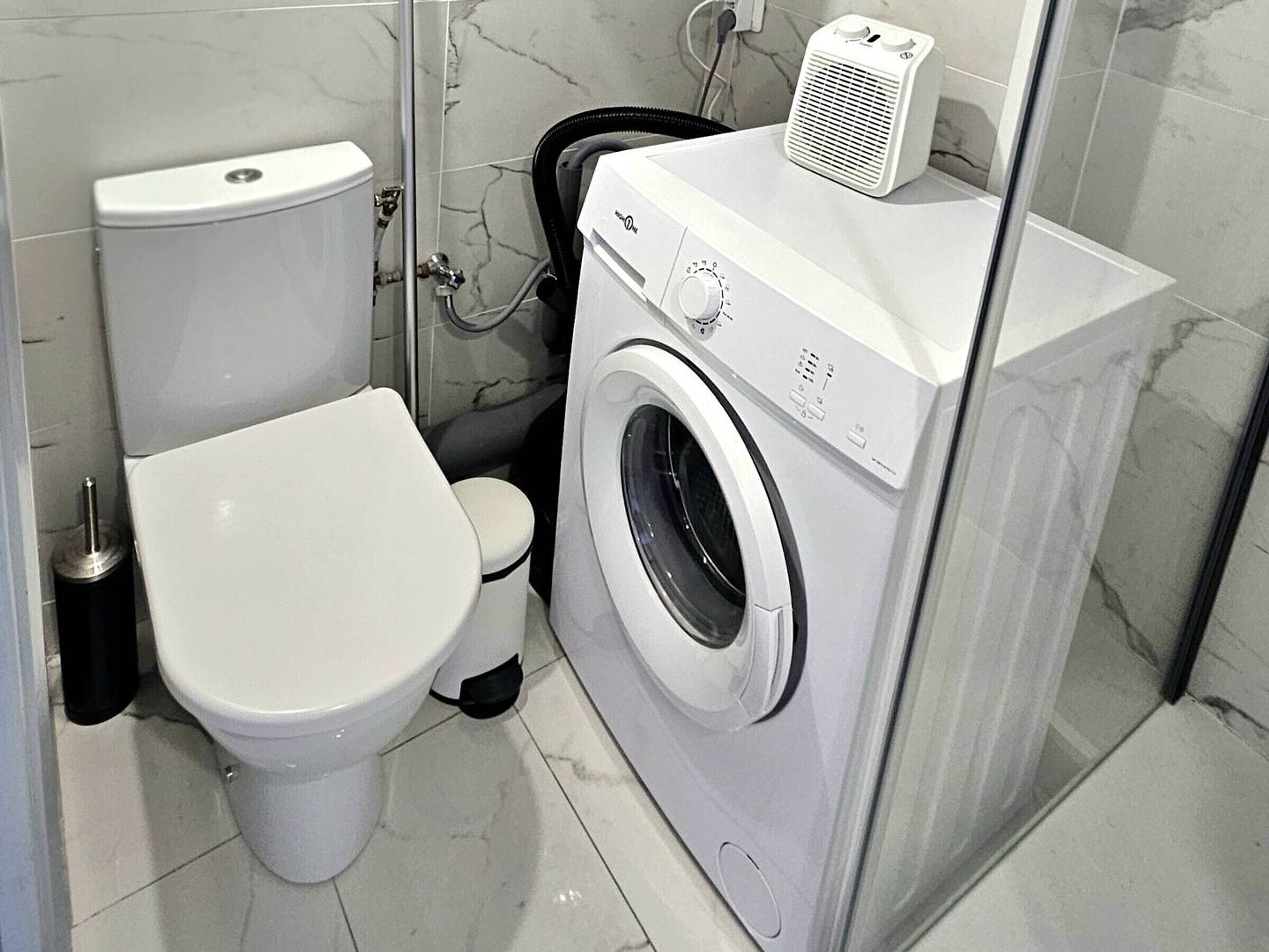 Une petite salle de bain comprenant des toilettes, un lave-linge et un espace douche.