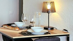 Ein Esstisch mit Tellern, Gläsern, Besteck, einem Glasbehälter und einem Baguette. Auf dem Tisch steht eine Lampe mit einem gemusterten Lampenschirm.