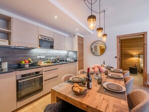 Eine moderne Küche mit integrierten Geräten, ein Essbereich mit einem Holztisch für sechs Personen und ein gemütlicher Wohnbereich mit Holzboden und Spiegel an der Wand.
