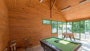 Une table de billard dans une pièce en bois, avec des chaises et une table de baby-foot.