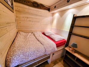 Ein kleiner, holzmöblierter Raum mit einem Einzelbett, einem Nachttisch und einem an der Wand befestigten Regal.