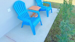 Two blue Adirondack chairs with a wooden table on a concrete patio next to a white wall. - Enjoyable 1-bedroom house in charming Lehigh Acres/Fort Myers (Lehigh Acres)