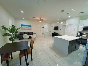 A modern kitchen with a central island, a dining area with a table and chairs, a living room with a sofa and a TV, and a large potted plant. - Enjoyable 1-bedroom house in charming Lehigh Acres/Fort Myers (Lehigh Acres)