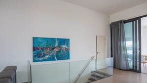 Un interno moderno con una scala in vetro, un divano grigio e un grande quadro astratto appeso alla parete.