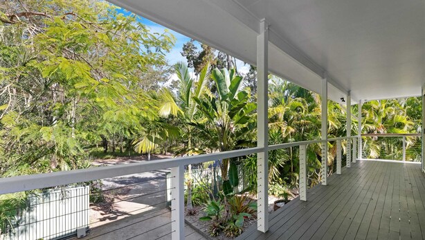 A covered outdoor area with a wooden deck, white railings, and lush tropical vegetation. - The Palms - Beach Retreat With Pool, Garden, BBQ (Toogoom)