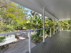 A covered outdoor area with a wooden deck, white railings, and lush tropical vegetation. - The Palms - Beach Retreat With Pool, Garden, BBQ (Toogoom)