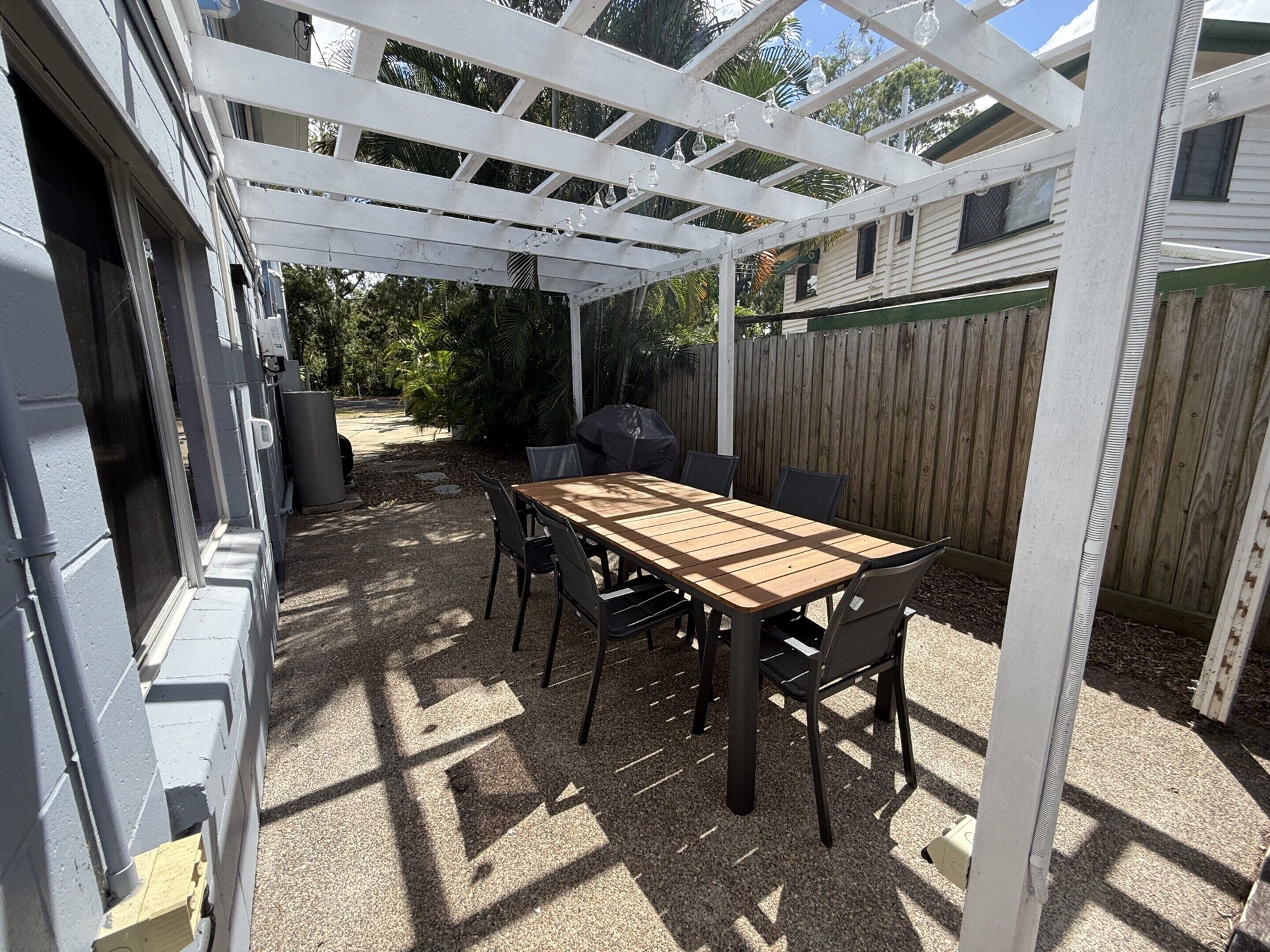 Une terrasse couverte avec une table et des chaises en bois, un barbecue et une clôture en bois.