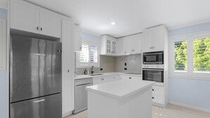 A modern kitchen with white cabinetry, stainless steel appliances, and a central island. - The Palms - Beach Retreat With Pool, Garden, BBQ (Toogoom)
