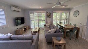 A modern living room with a sofa, a coffee table, a TV, and a dining area with a table and chairs. - The Palms - Beach Retreat With Pool, Garden, BBQ (Toogoom)