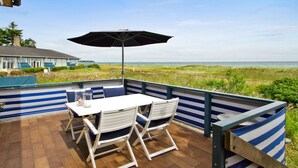 Une terrasse avec une table et des chaises, un grand parasol et une vue sur la plage.