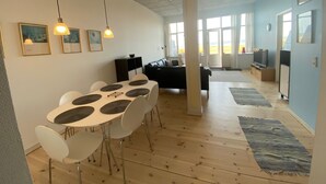 Un salon moderne avec un coin repas, de grandes fenêtres et un téléviseur à écran plat.