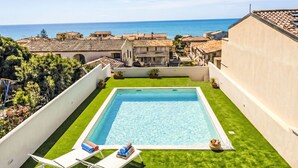 Ein Swimmingpool mit Blick auf das Meer, umgeben von Gebäuden im mediterranen Stil.
