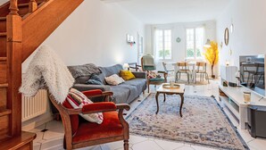 Ein geräumiges Wohnzimmer mit einer Holztreppe, einem Sofa, einem roten Sessel, einem Couchtisch und einem Essbereich mit Tisch und Stühlen.