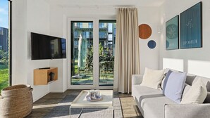 Uma sala de estar moderna com televisão de tela plana, um sofá, uma mesa de centro e vista para uma varanda com móveis de exterior.