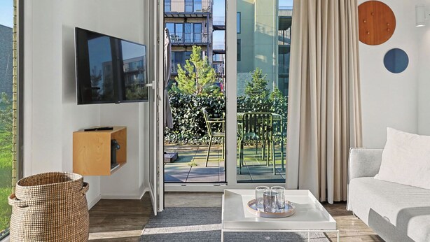 Uma sala de estar moderna com televisão de tela plana, um sofá, uma mesa de centro e uma porta de vidro deslizante que dá para uma varanda externa.