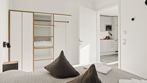 Quarto com cama, almofadas, guarda-roupa e vista para uma cozinha.