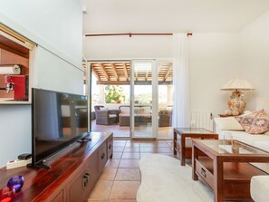 Een woonkamer met een televisie, houten meubels, een bank, een glazen salontafel en een glazen schuifdeur die leidt naar een terras.