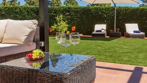 Une terrasse avec des meubles en osier, une table en verre avec des verres à vin et un parasol blanc.