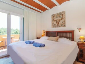 Een slaapkamer met een groot bed, een houten hoofdbord, een schilderij aan de muur en een balkon met uitzicht.