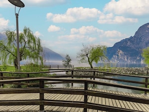 A wooden bridge over a calm body of water, surrounded by trees and mountains in the background. - Apartment Ilaria by Interhome (Riva del Garda)