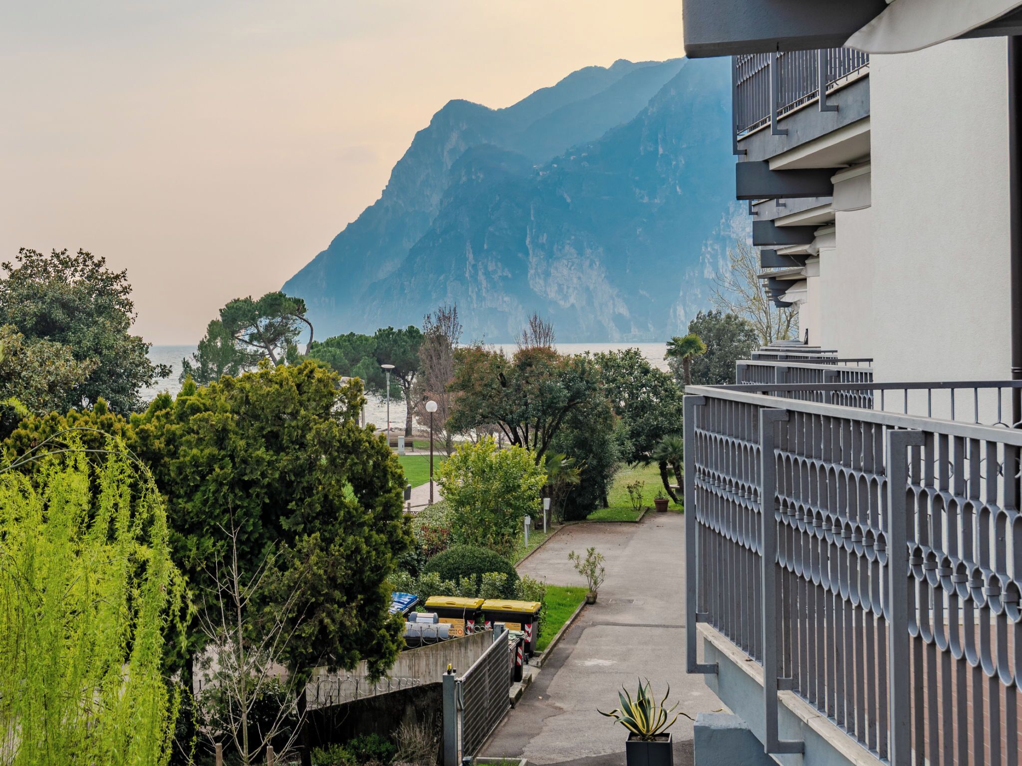 A residential area with a mountain in the background, a paved walkway, and a building with a balcony.