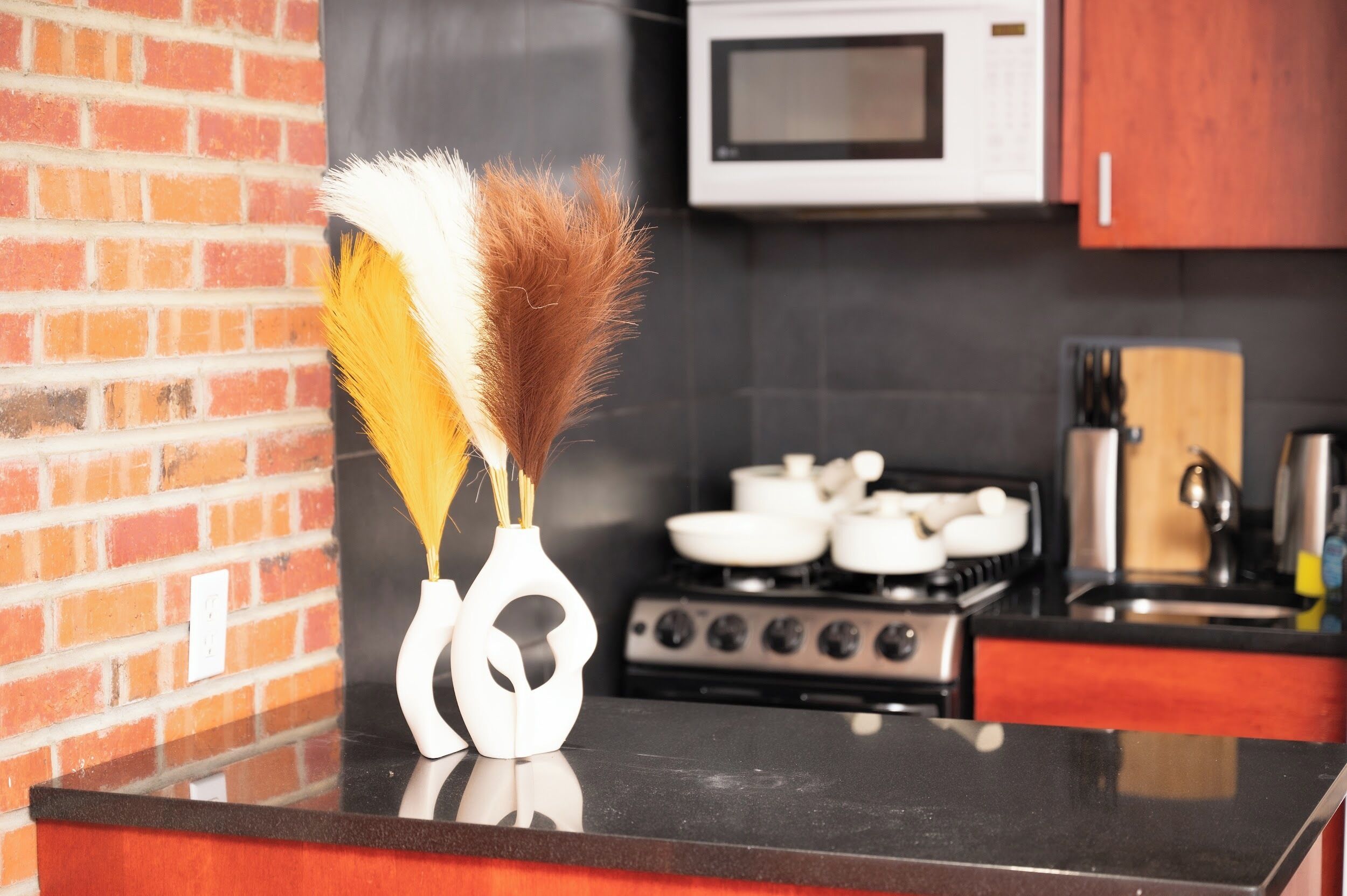 A kitchen with a black countertop, a white vase with feathers, a microwave, and a stove.