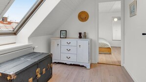 Une chambre avec un plafond en pente, une commode blanche, un lit, une décoration murale ronde en fibres tressées et un puits de lumière.