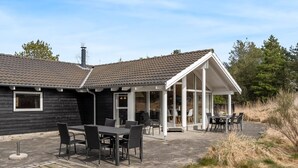 Moderni talo, jossa on patio, jossa on pöytä ja tuoleja, katettu oleskelualue ja savupiippu.