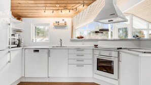 Moderni keittiö, jossa on valkoiset kaapit, sisäänrakennettu uuni ja ikkuna, josta avautuu näkymä vehreään maisemaan.