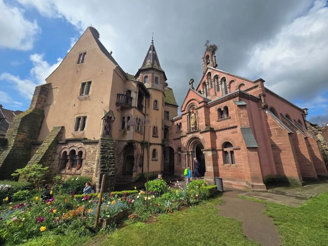 Il s’agit d’un bâtiment historique doté d’un toit à forte pente, d’une tour imposante et d’un jardin bien entretenu où poussent différentes espèces de fleurs.